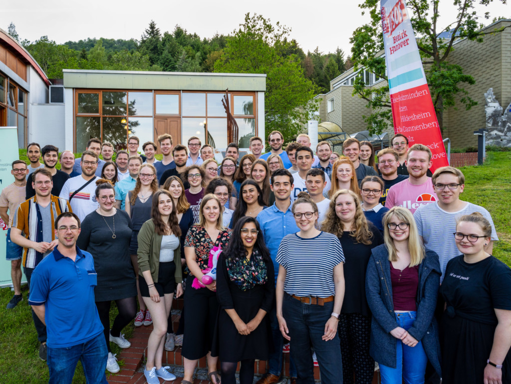 Man sieht eine Gruppe von lächelnden, jungen Menschen vor einem Tagungszentrum. Man sieht hinten rechts eine Flagge auf der "Jusos Bezirk Hannover" steht.